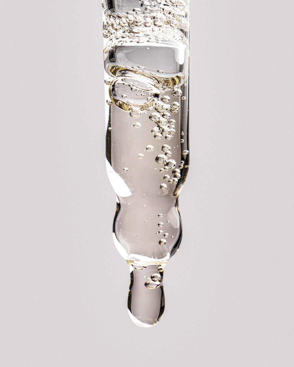 Close-up of glass pipette dropper dispensing a drop of clear PDRN scalp serum
