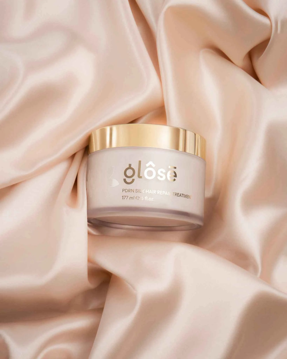 Glôsē PDRN Silk Hair Repair Treatment jar resting on draped blush silk fabric